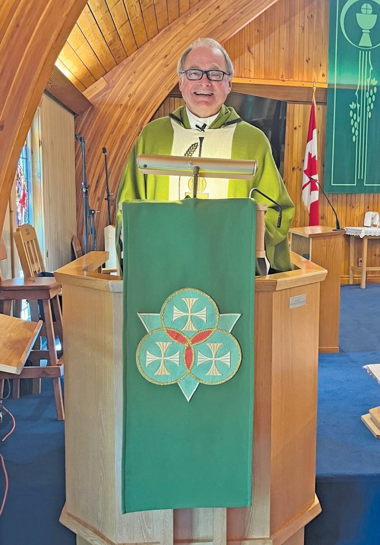 A man wearing glasses and a green chasuble standing in a pulpit in a wooden church