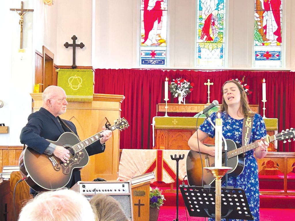a man and a woman play guitar and sing at the fron tof a church with red carpet and curtains