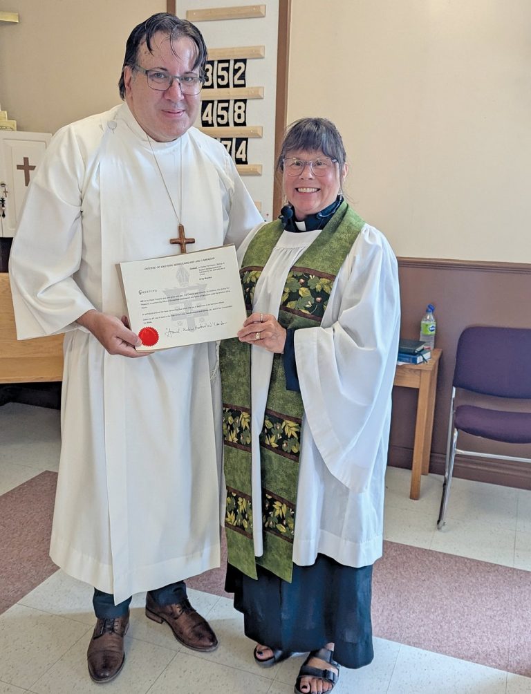 A man dressed in white alb receives a certificate from a woman, dressed in a surplice and green stole