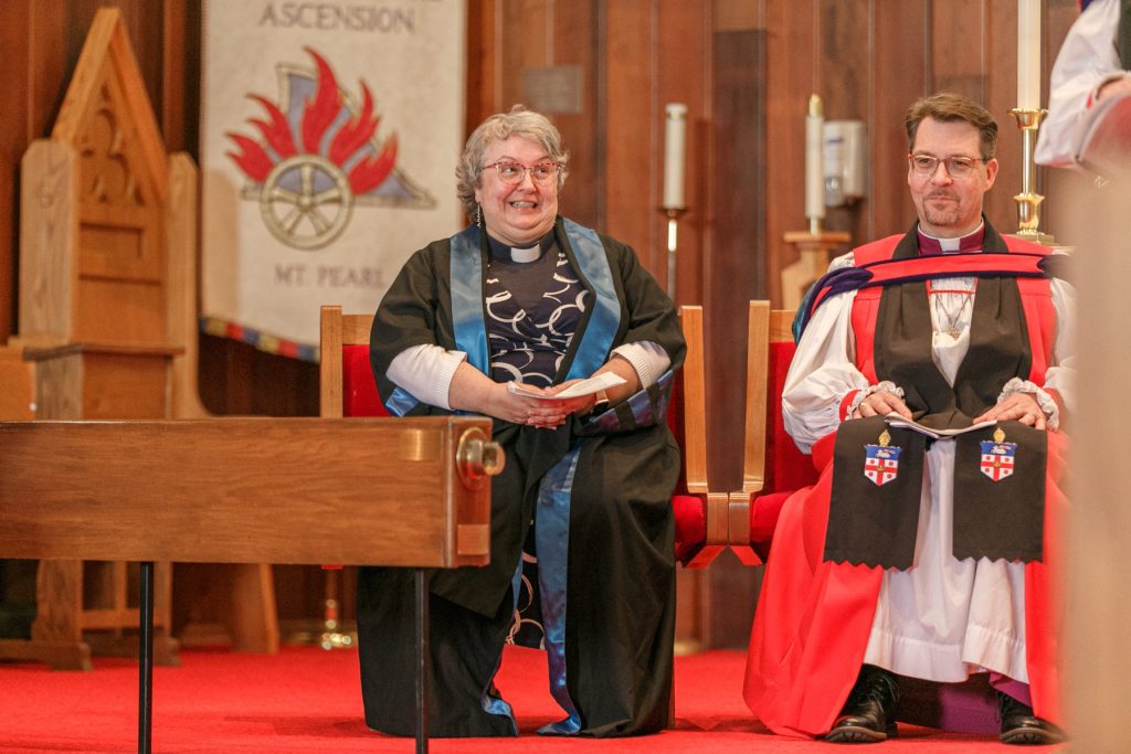 Woman and man in clergy vestments seated during a service inside a church.