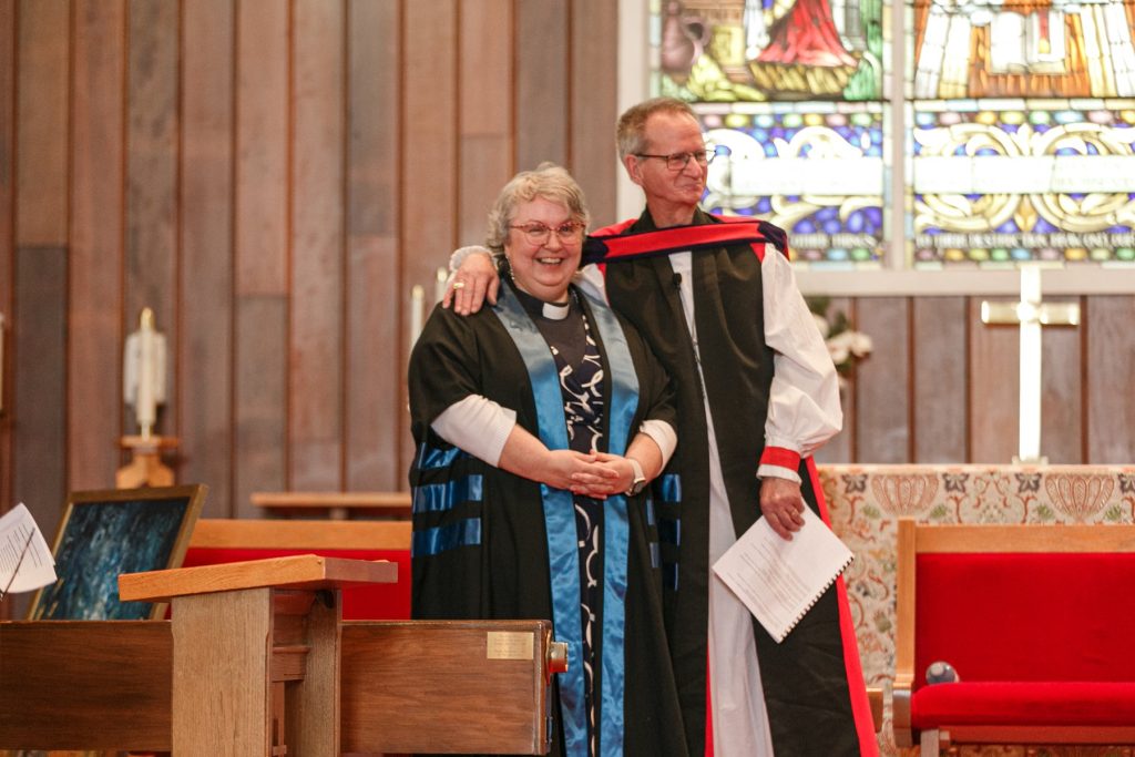 Woman and man in clergy vestments smiling together near the church altar.