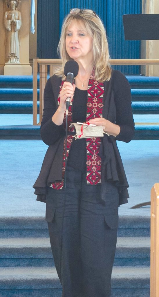 a woman with a microphone speaks at the front of a church that has blue carpet