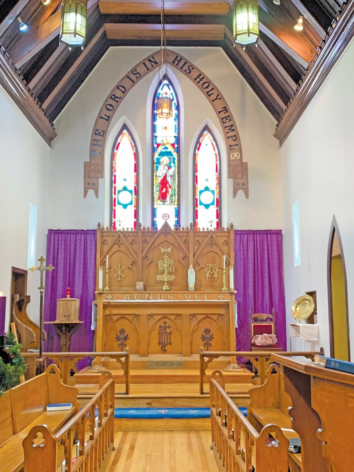 interior of a wooden church with purple hangings. Above the altar are painted the words: "The Lord Is In His Holy Temple."