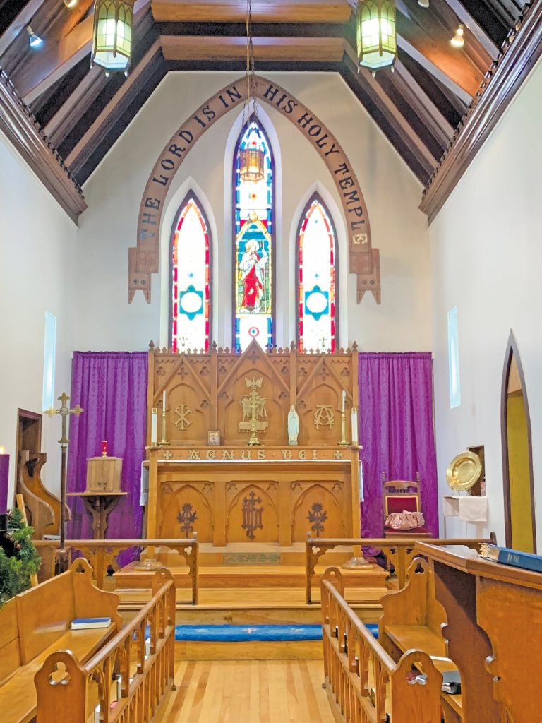 interior of a wooden church with purple hangings. Above the altar are painted the words: "The Lord Is In His Holy Temple."