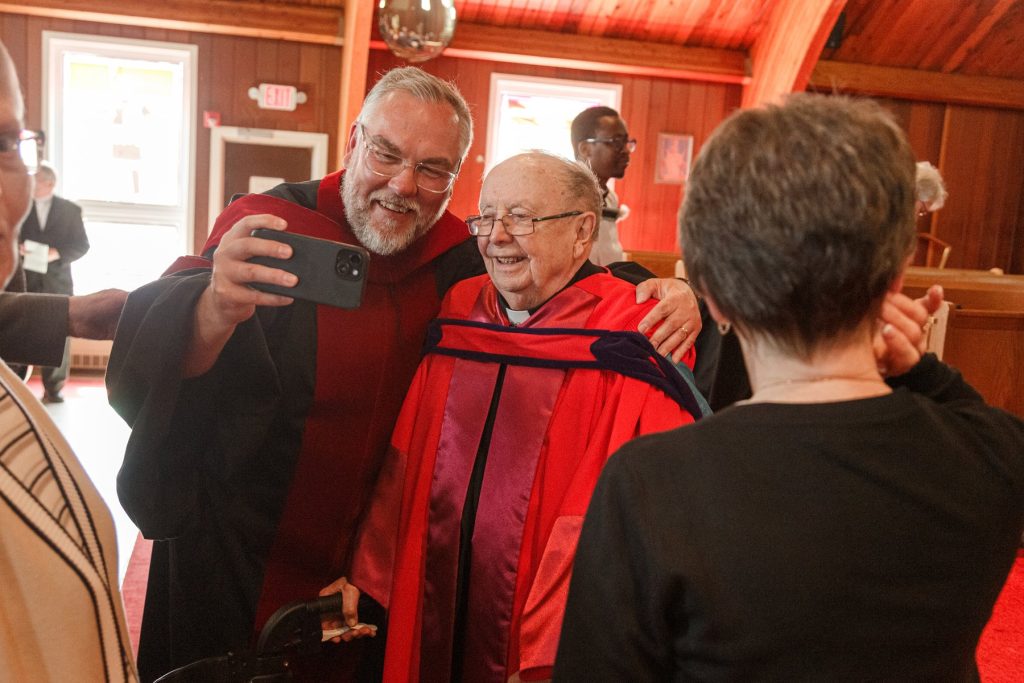 Man taking a selfie with an elderly man using a walker inside a church.
