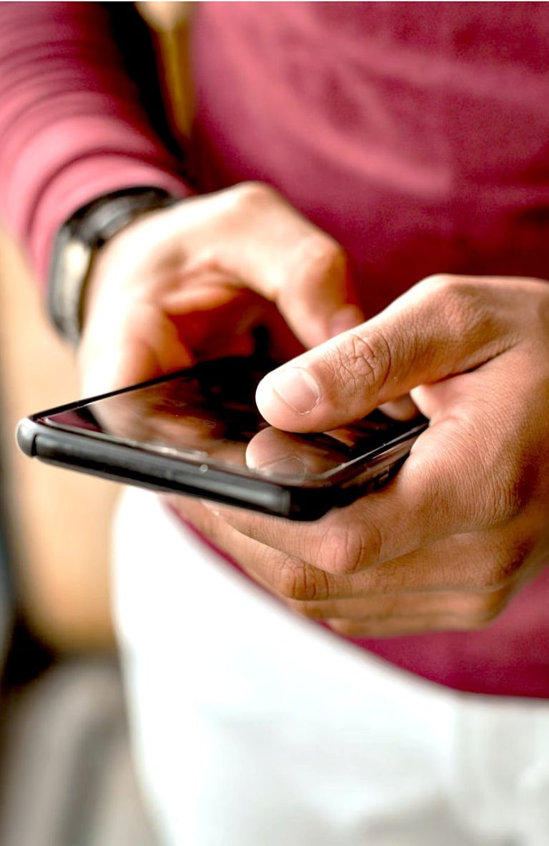 a person with a dark rose shirt and white trousers looks at a cell phone