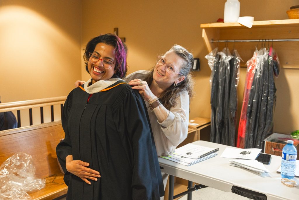Woman helping another woman adjust her graduation gown.