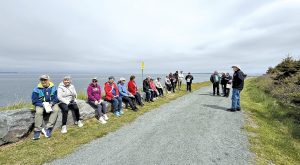 A group sitting along a coastal path listening to a speaker outdoors.