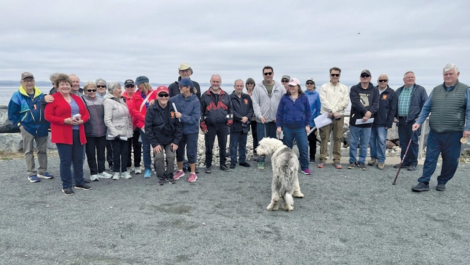 A large group of people and a dog standing along a coastal gravel path.
