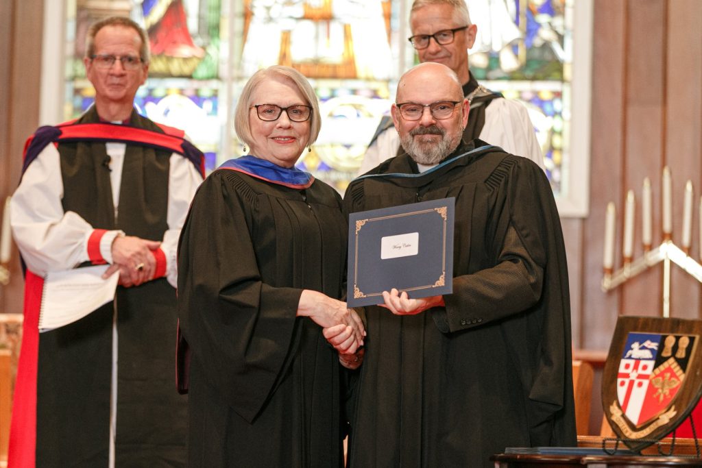 Man presenting a certificate to a woman in graduation robes.