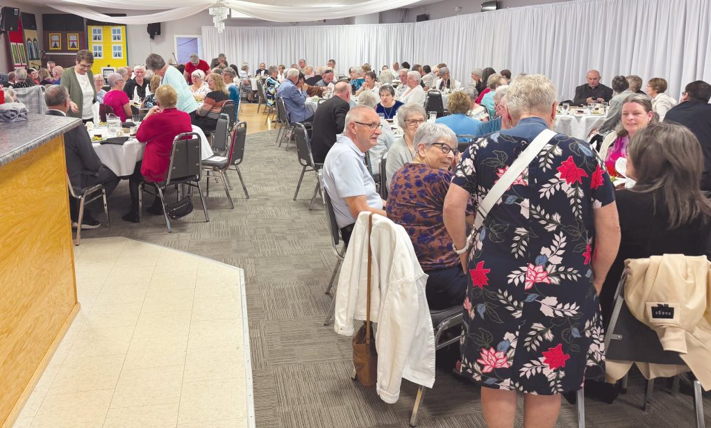 a group of people sitting at folding tables in a church hall