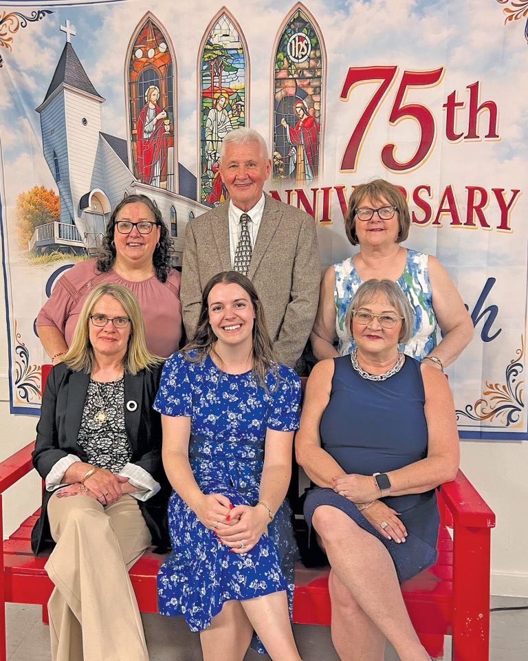 a group of 6 people pose in front of a ban ner that says "75th Anniversary" on it