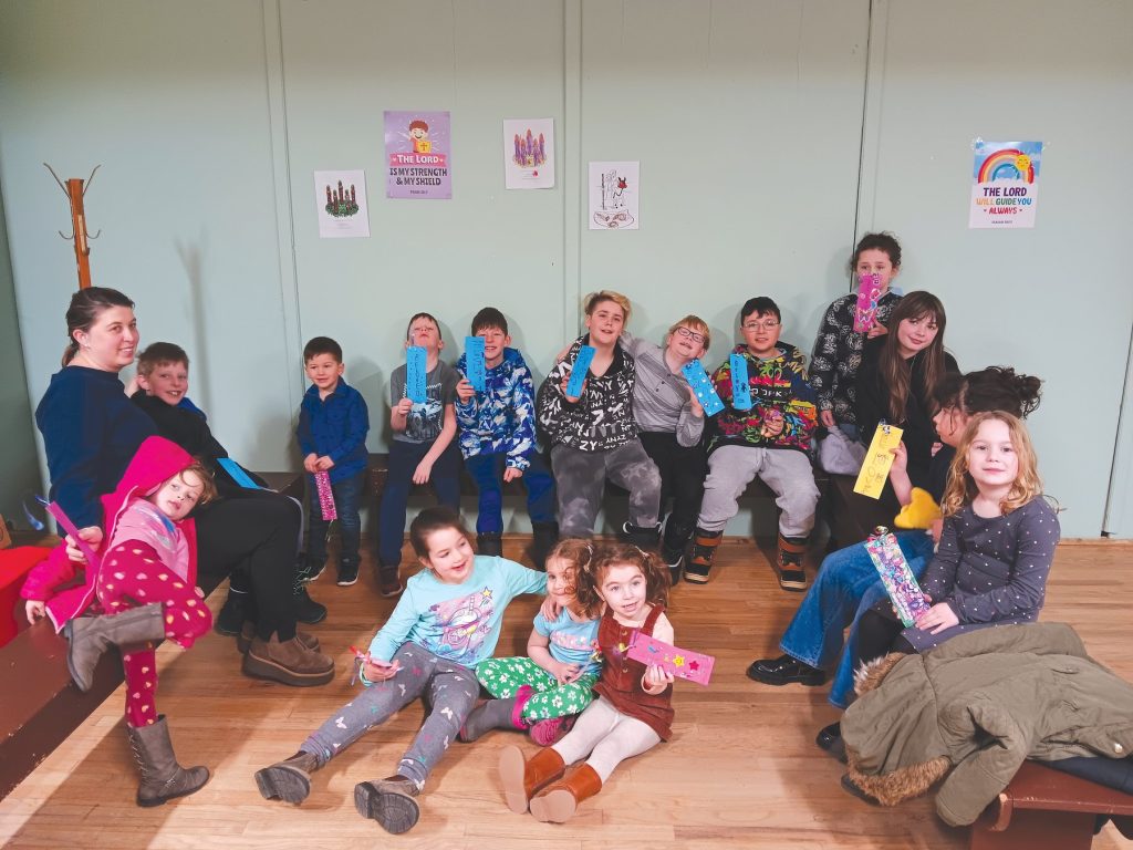 Children and adults sitting together holding decorated craft bookmarks.