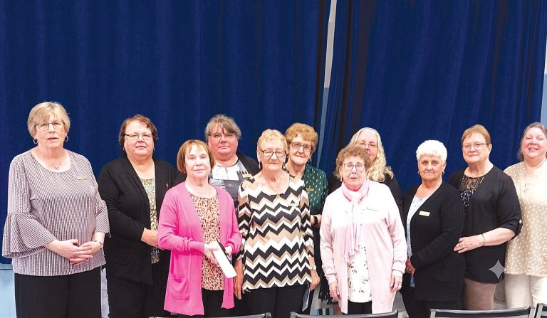 Group photo of ten women standing together in front of a blue curtain.