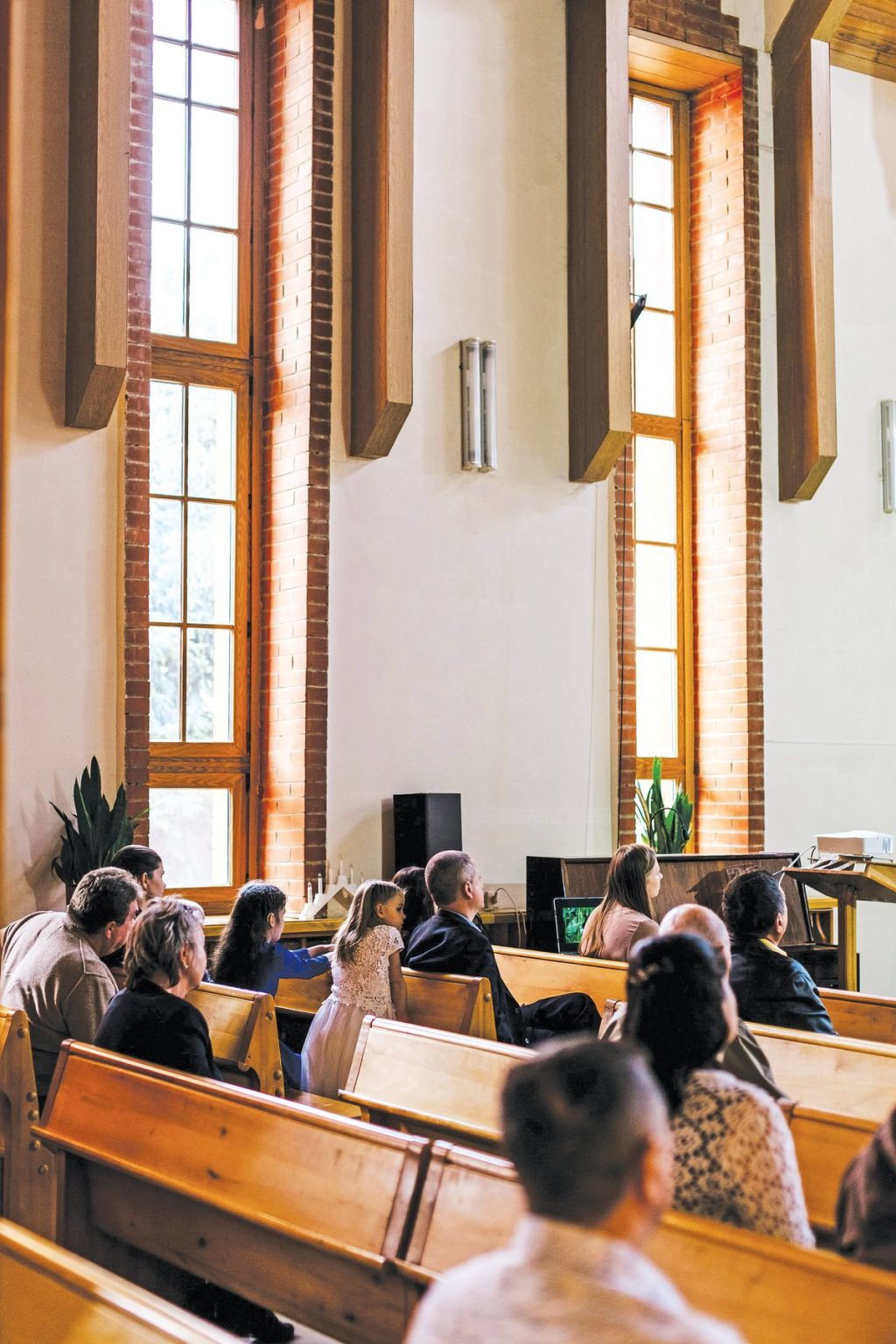 People sitting in wooden pews inside a church with tall windows.