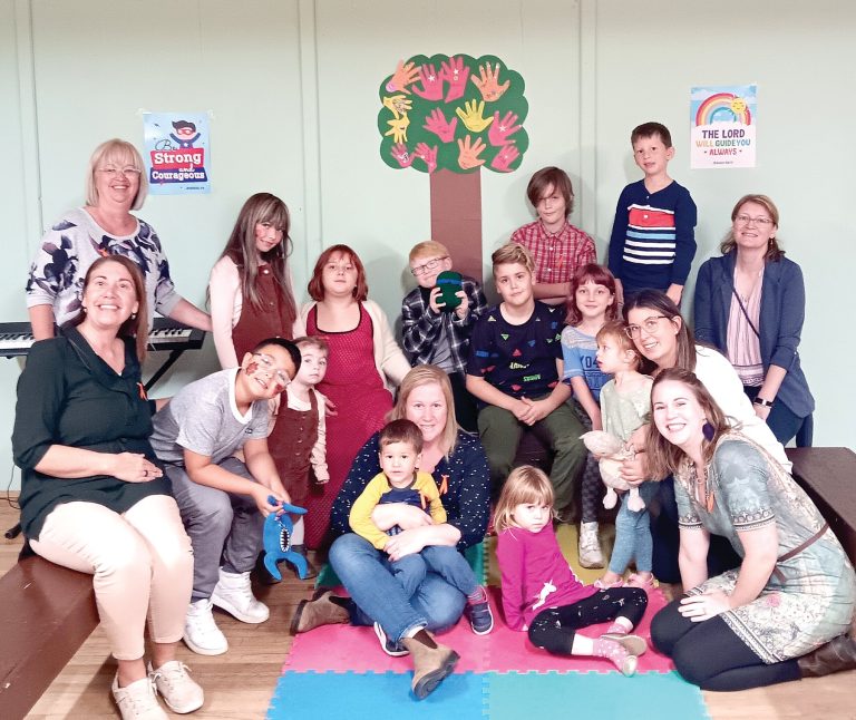 Group photo of children and adults gathered together in front of a handprint tree banner.