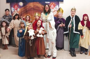 Group of children and adults in a nativity play wearing costume robes and crowns.