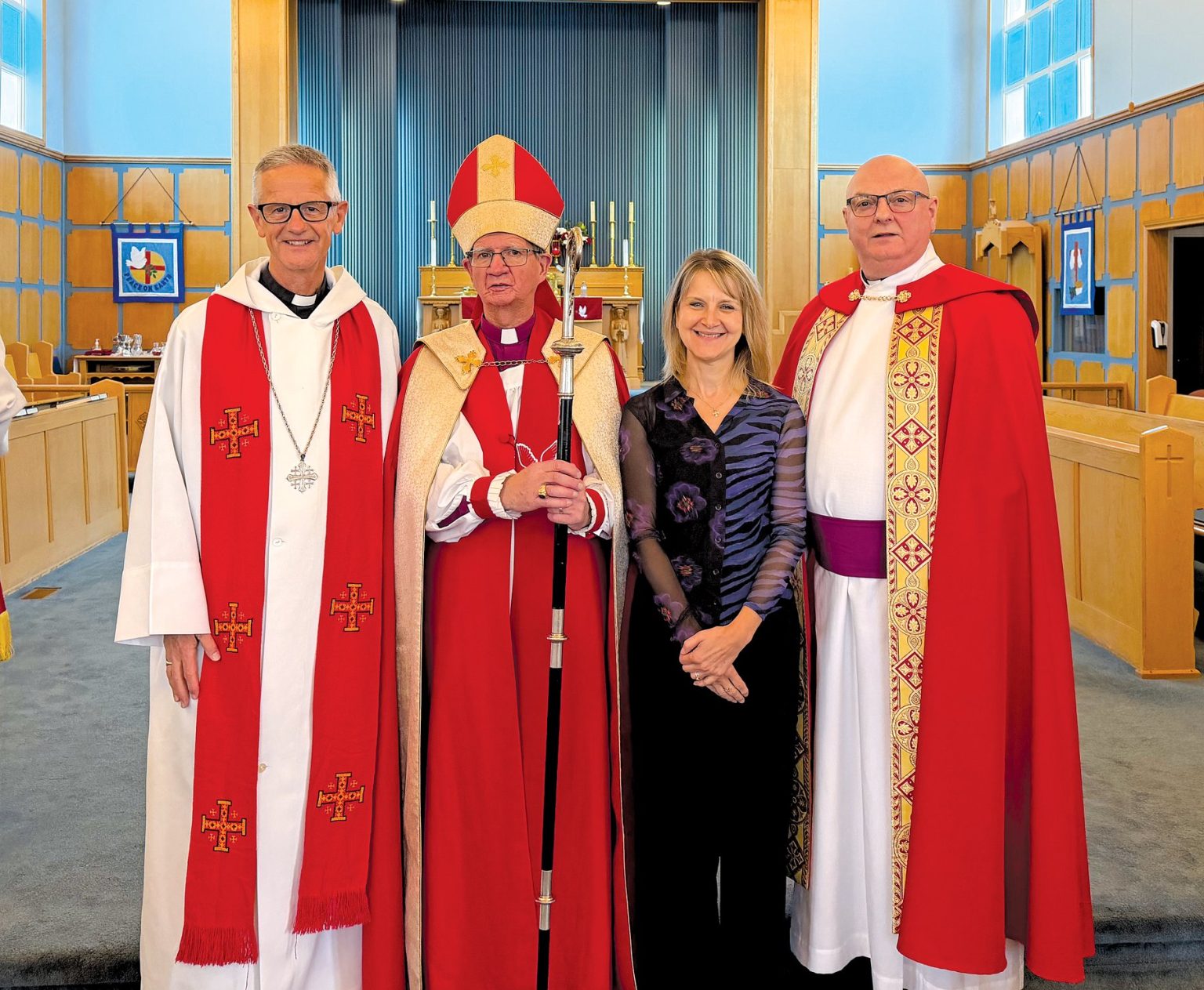 three men and one women at the front of a church; the men are vested as clergy