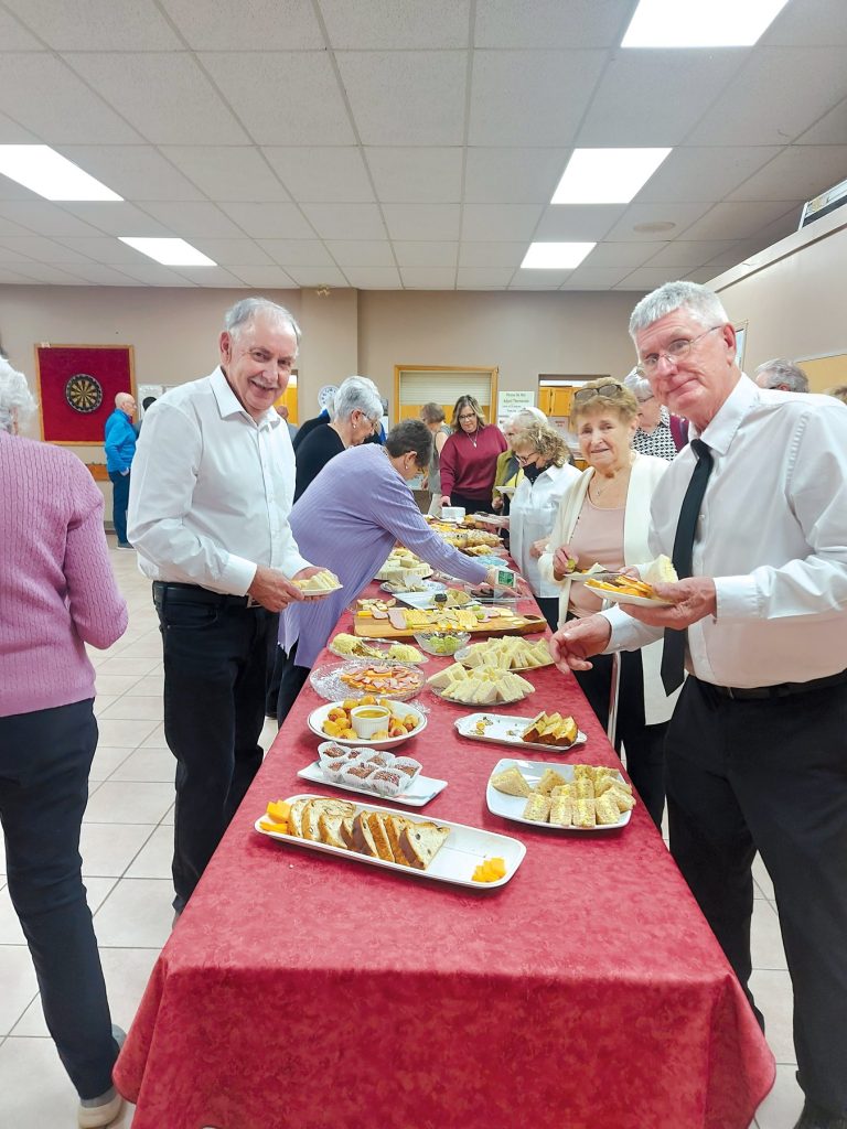 People gathered around a buffet table filled with sandwiches and snacks.