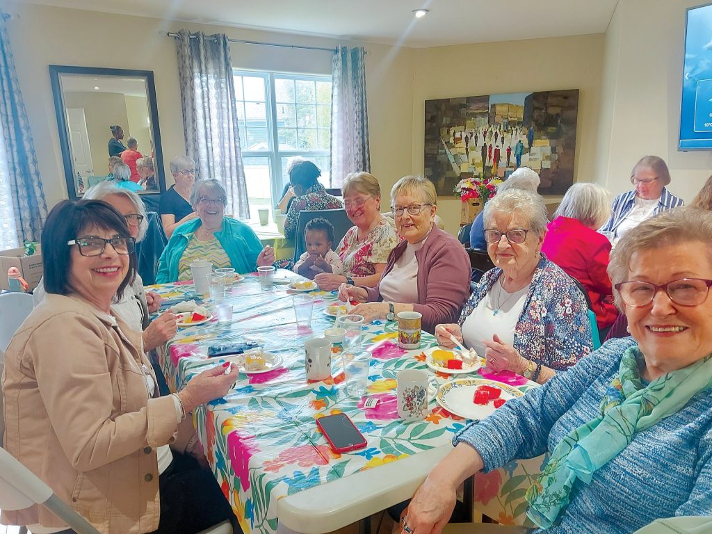 A group of women sit around a table, smiling at the camera