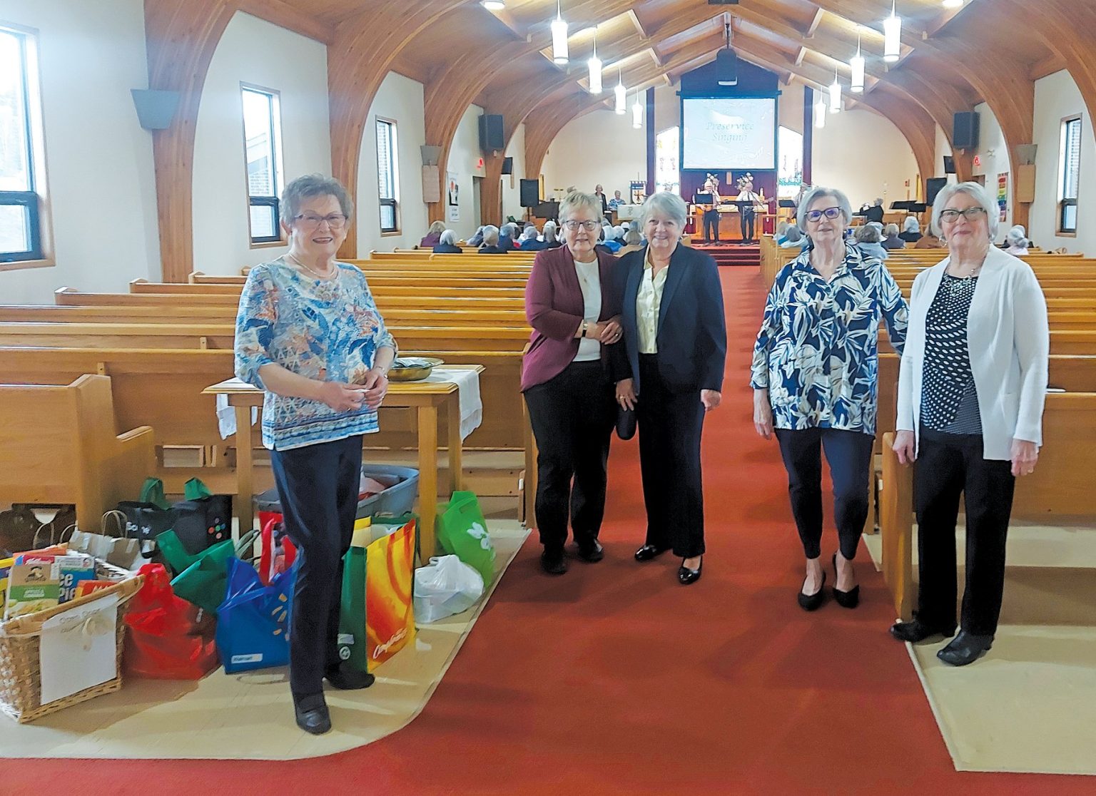 Five women standing in a church aisle near wooden pews and gift bags.