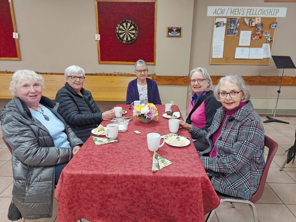 Five women sitting around a table with drinks and snacks.