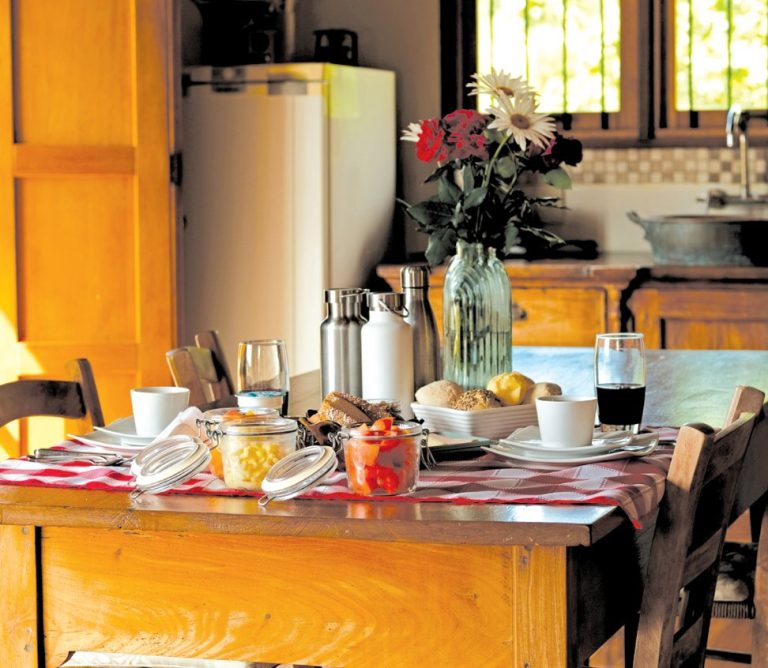 a wooden kitchen table set for a meal, including a red and white tablecloth.