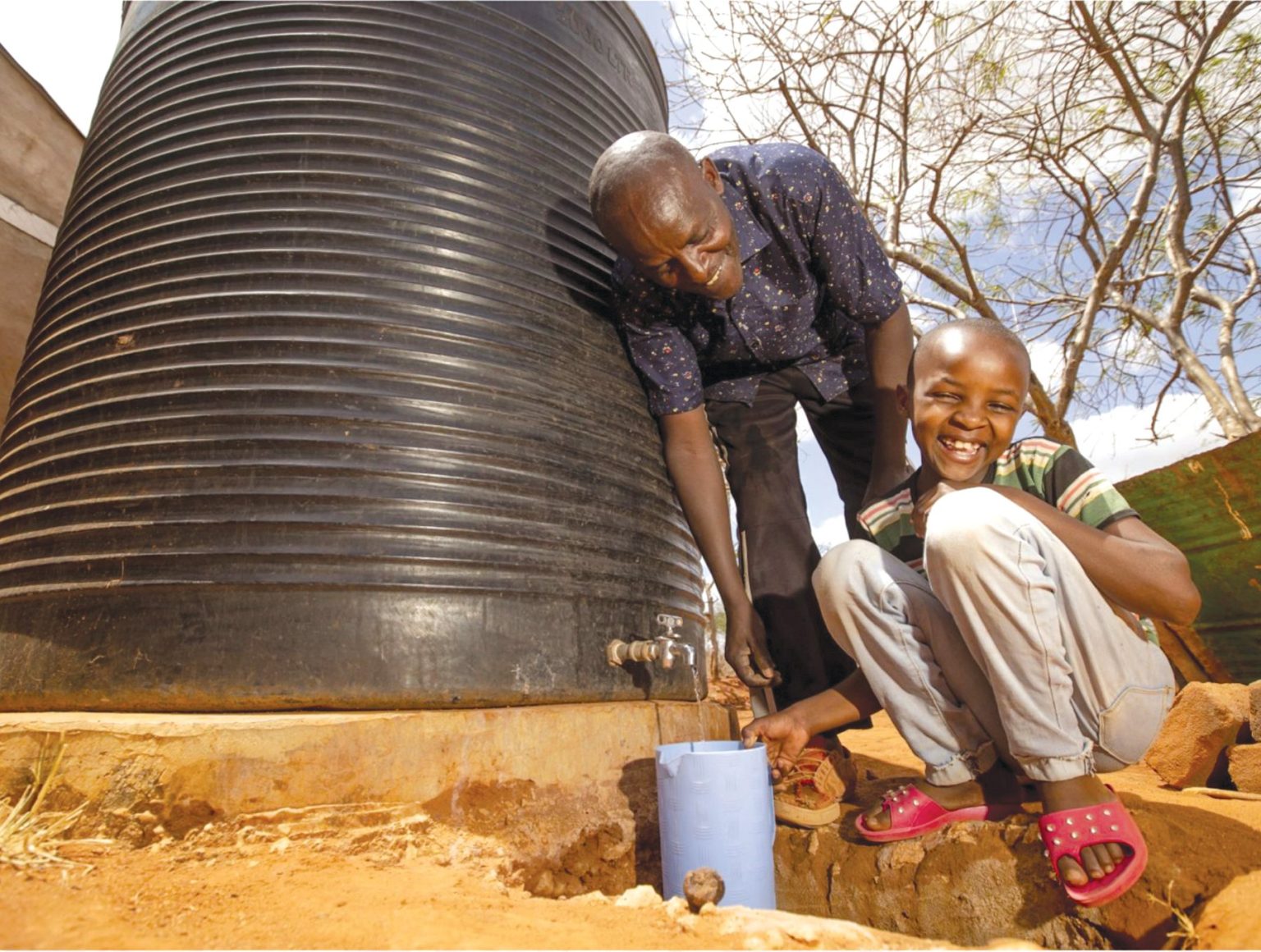Two people smile as clean water pours from a large metal tank