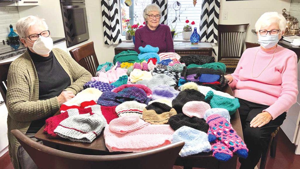 Women in front of a selection of knitted goods.
