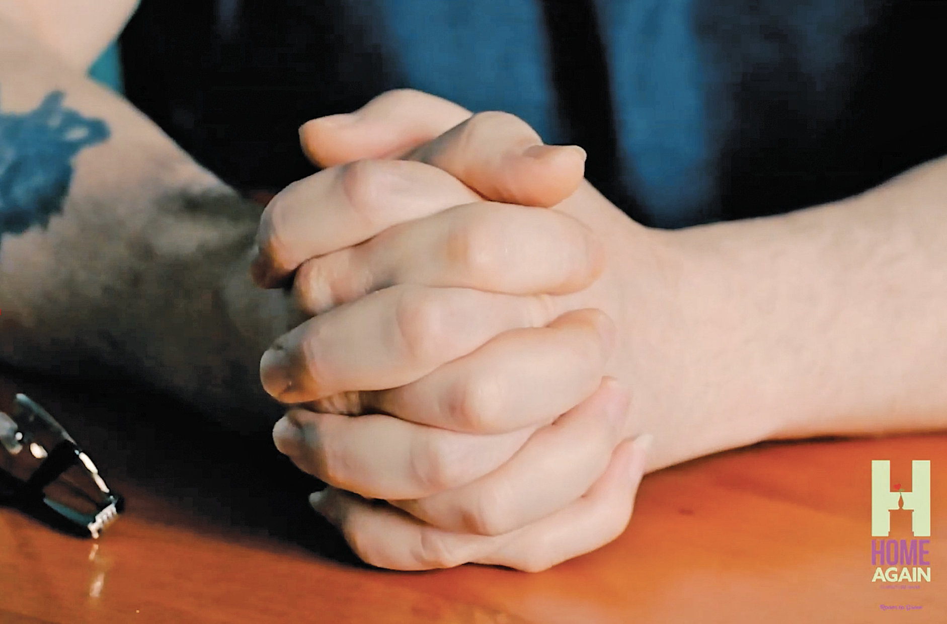 man's hands resting on a wooden table